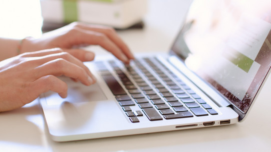 Arbeit am Laptop Studentin tippend am Laptop, daneben liegen Bücher.
