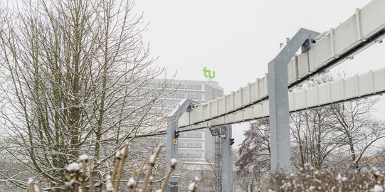 Bare bushes in the foreground, H-Bahn track and the mathematics building in the snow in the background.